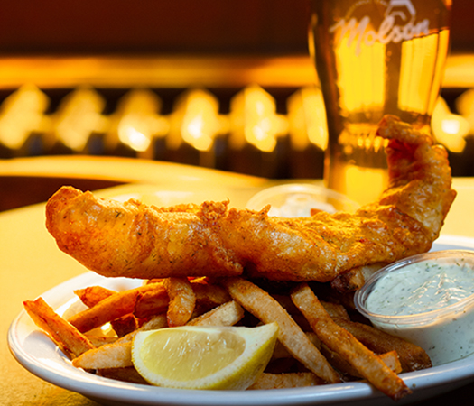 A plate of fish and chips with a draft beer.