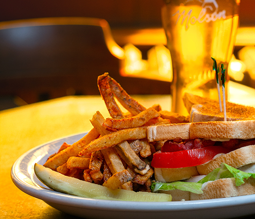 Une assiette avec un sandwich club, des frites et une bière en fût.